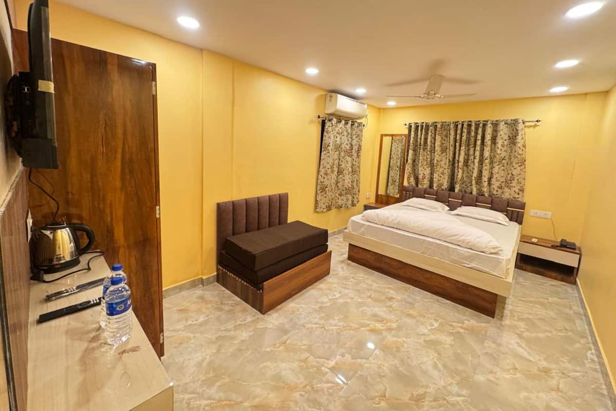 Un dormitorio con cama, armario de madera, pequeño sofá, televisor, botella de agua y ventilador de techo.
