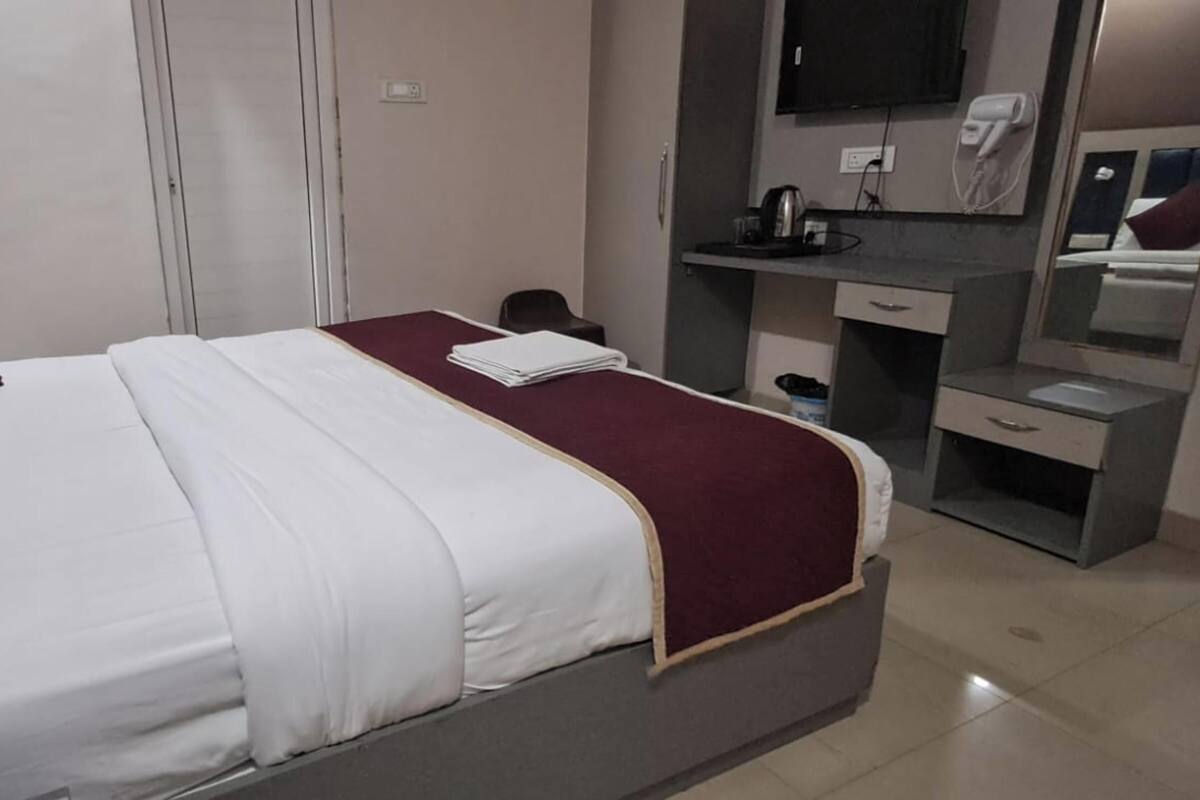 Una habitació d'hotel amb un llit, escriptori, mirall, televisió i armari.