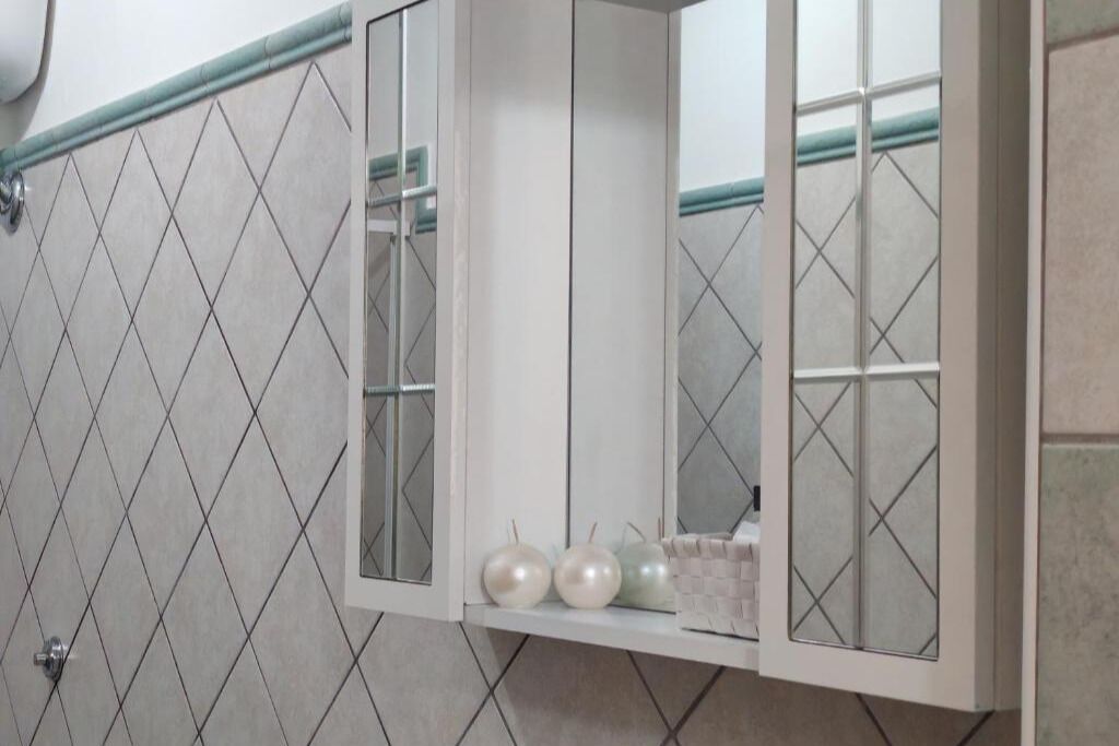 Un baño con pared de azulejos, un mueble de espejo y un perchero para toallas.