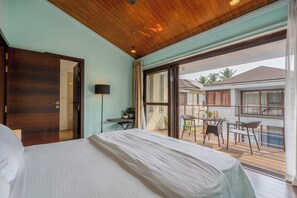 A bedroom with a large bed, a desk with a lamp, and a balcony with a table and chairs. - Staymaster Casa Amaira 3BR Villa  (Vagator)