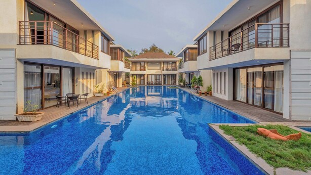 A modern hotel with a central swimming pool, balconies, and a clear view of the building's architecture. - Staymaster Casa Amaira 3BR Villa  (Vagator)