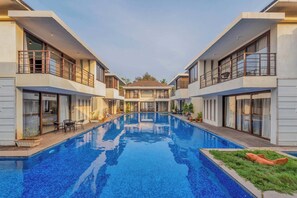 A modern hotel with a central swimming pool, balconies, and a clear view of the building's architecture. - Staymaster Casa Amaira 3BR Villa  (Vagator)