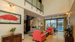 A spacious living area with a staircase, a dining area, and a large window with a view. - Staymaster Casa Amaira 3BR Villa  (Vagator)
