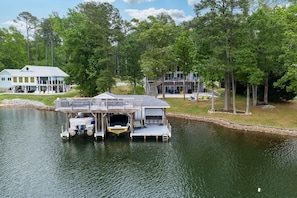 A lakeside property with a dock, a large house, and a boat. - NEW! Family Lake Gaston Getaway 🛶 5BR • Dock • Kayaks • Flat Waterfront Lot (Littleton)