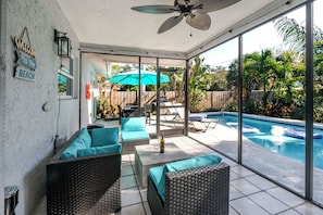 Eine überdachte Terrasse mit Korbmöbeln, einem Pool und Blick auf den Garten.
