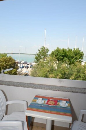 Een balkon met een tafel en stoelen, met uitzicht op een jachthaven vol boten en een heldere lucht.