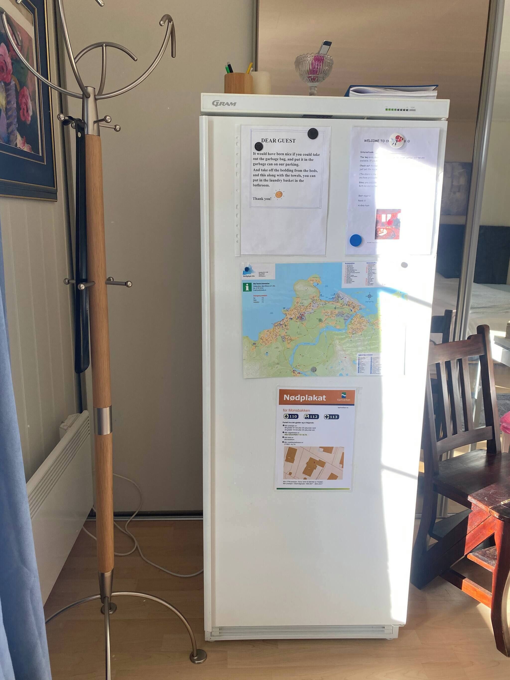 A white refrigerator with a map and a welcome sign, a wooden chair, and a metal stand.