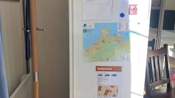 A white refrigerator with a map and a welcome sign, a wooden chair, and a metal stand.