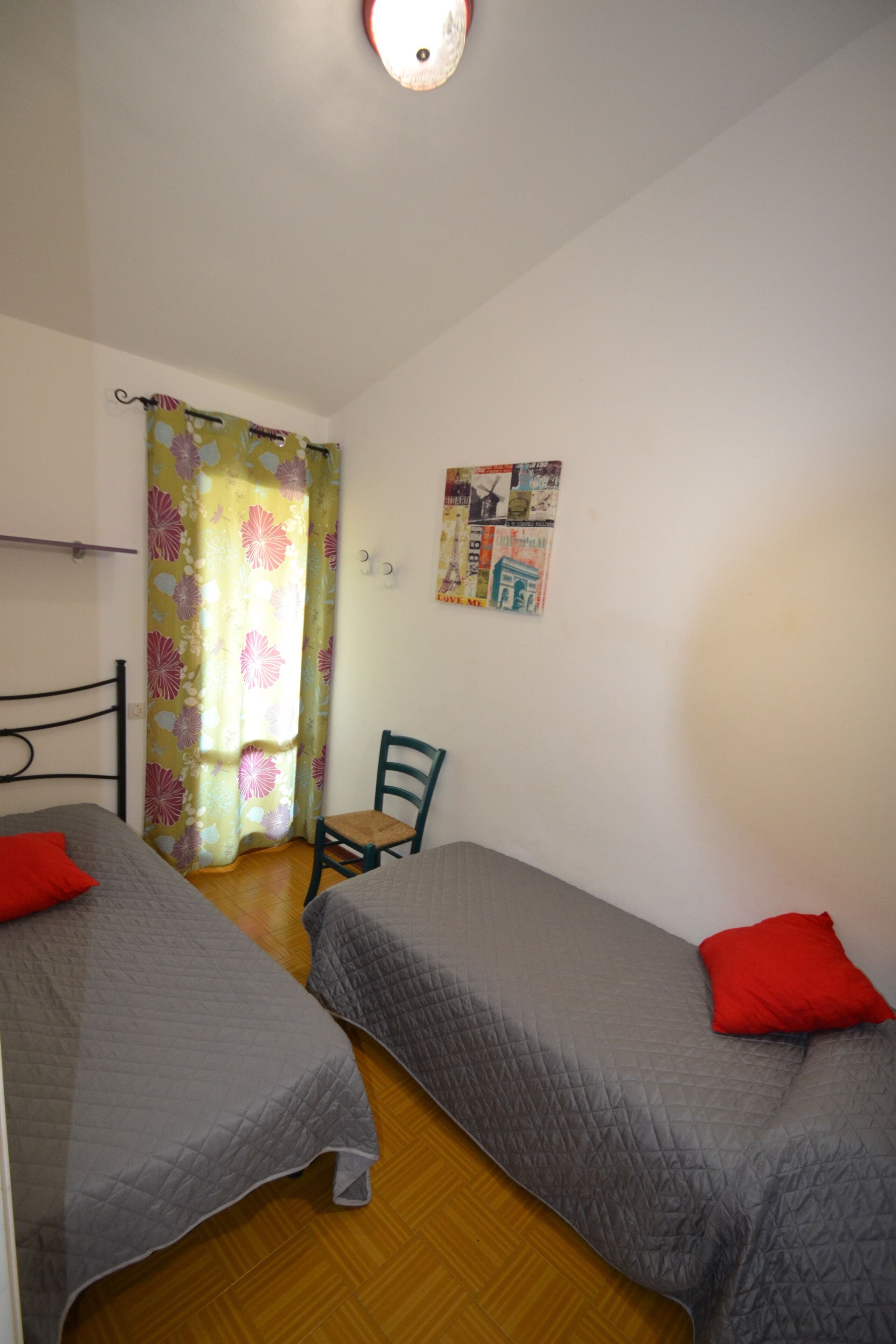 A room with two beds, a chair, a curtain, and a wall with a poster.