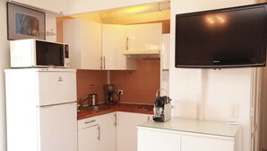 Une cuisine compacte avec des meubles blancs, un four à micro-ondes, une machine à café et un téléviseur à écran plat.