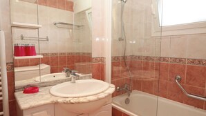 Une salle de bain avec un lavabo, un miroir, une douche et une fenêtre.