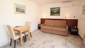 Une pièce comprenant une table à manger en bois, des chaises de couleur beige, un canapé beige, deux lampes fixées au mur et deux tableaux encadrés.