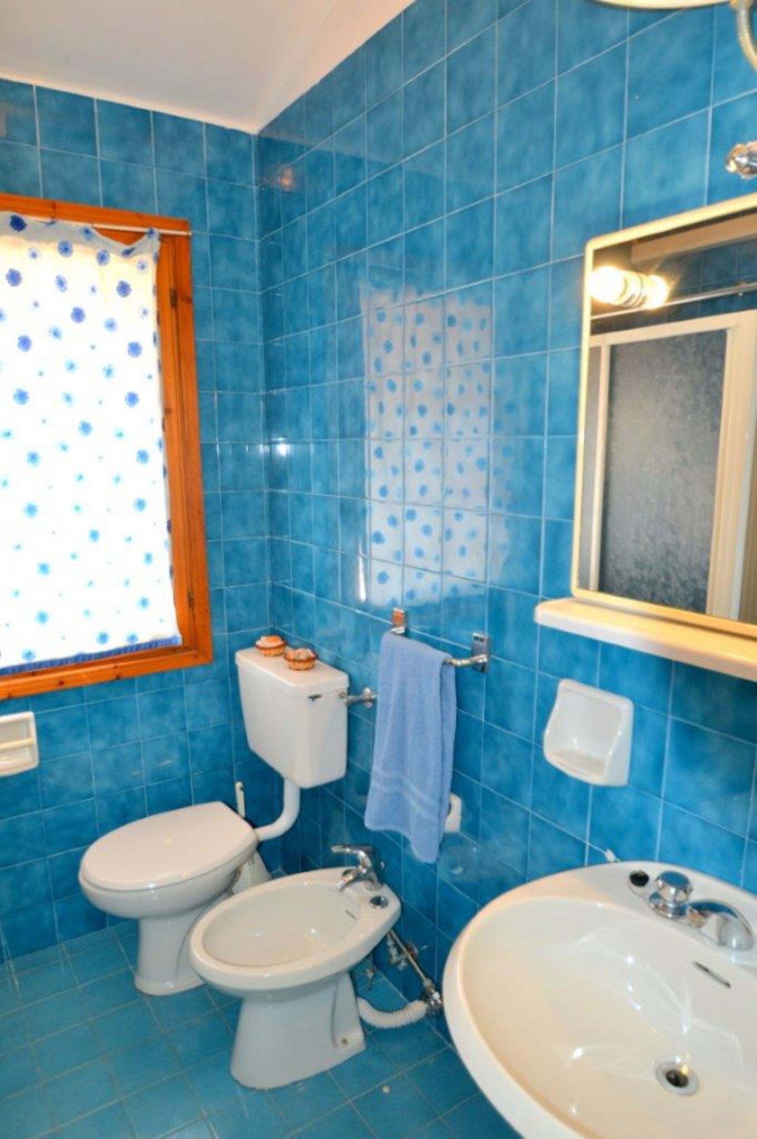 Un baño con azulejos azules, inodoro, bidé, lavamanos y espejo.