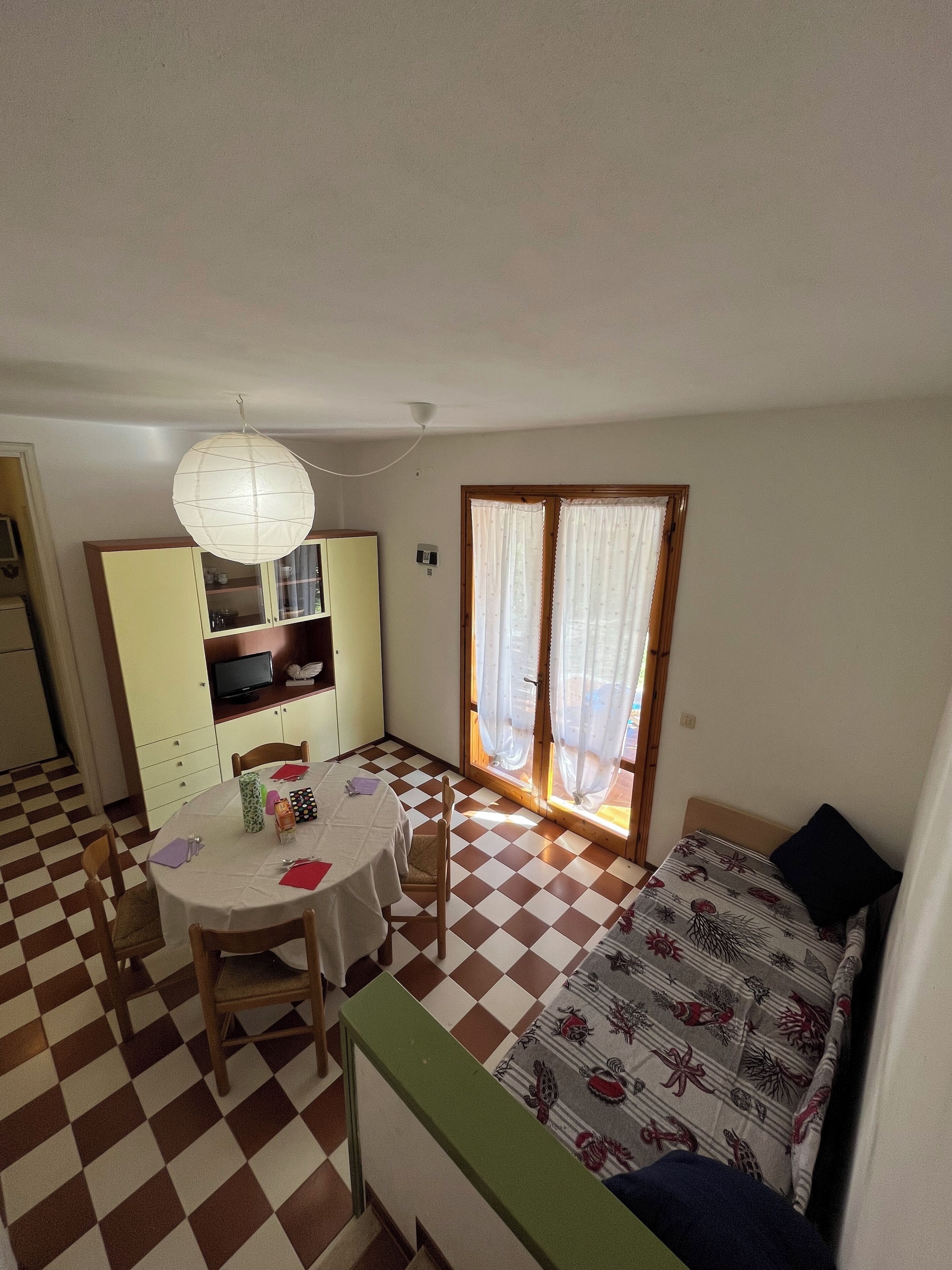 A compact room with a dining table, chairs, a sofa, a television, and a window with curtains.