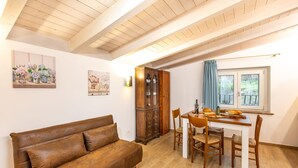 Ein gemütliches Wohnzimmer mit einem braunen Ledersofa, einem Essbereich mit Holztisch und -stühlen, einem Schrank und einem Fenster mit Aussicht.