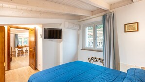 Ein Schlafzimmer mit einem großen Bett, einem an der Wand montierten Fernseher, einem Fenster mit Vorhängen und einer Tür, die auf einen Balkon führt.