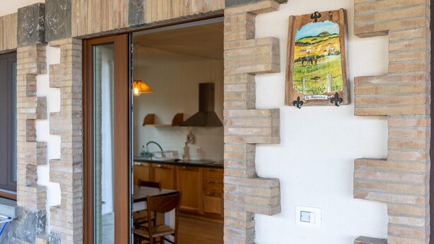 A kitchen with a wooden table and chairs, a hanging light fixture, and a rustic brick wall. - Le Vigne - Appartamento La Maremma (Bolsena)