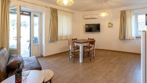 A living room with a sofa, a dining table with chairs, a TV, and an air conditioning unit. - Le Vigne - Appartamento La Maremma (Bolsena)
