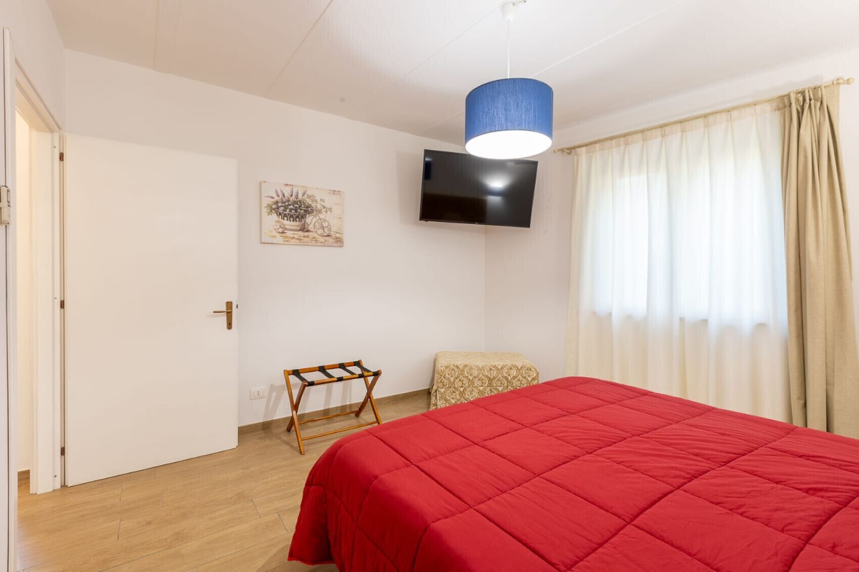 A room with a bed, a television, a door, a small table, and a window with curtains.
