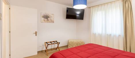 A room with a bed, a television, a door, a small table, and a window with curtains.