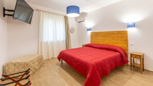 A bedroom with a wooden headboard, a bed with red bedding, a small wooden nightstand, a television mounted on the wall, and a window with curtains. - Le Vigne - Appartamento La Maremma (Bolsena)