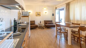 A compact kitchen with modern appliances, a dining area with a wooden table and chairs, a sofa, and a small side table. - Le Vigne - Appartamento La Maremma (Bolsena)