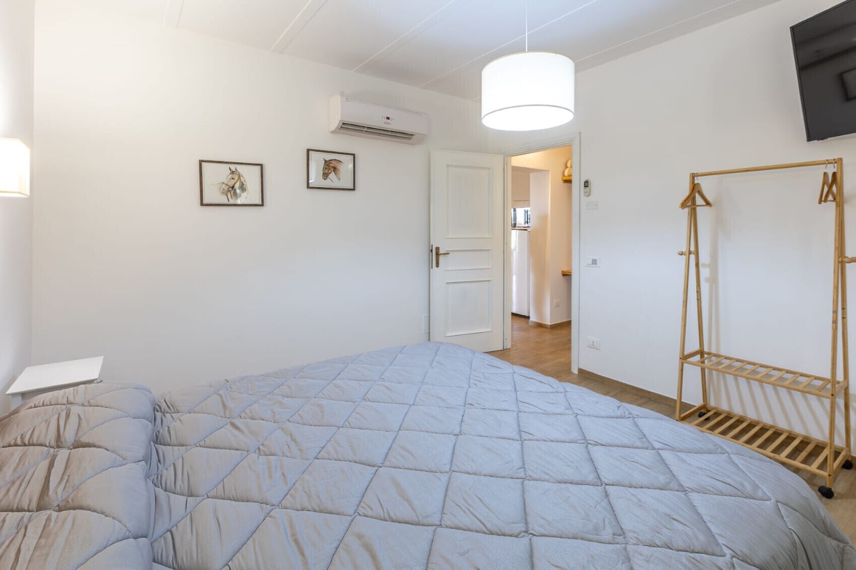 Ein Schlafzimmer mit Bett, einer Hängelampe, einer Klimaanlage und einem Wäscheständer aus Holz.