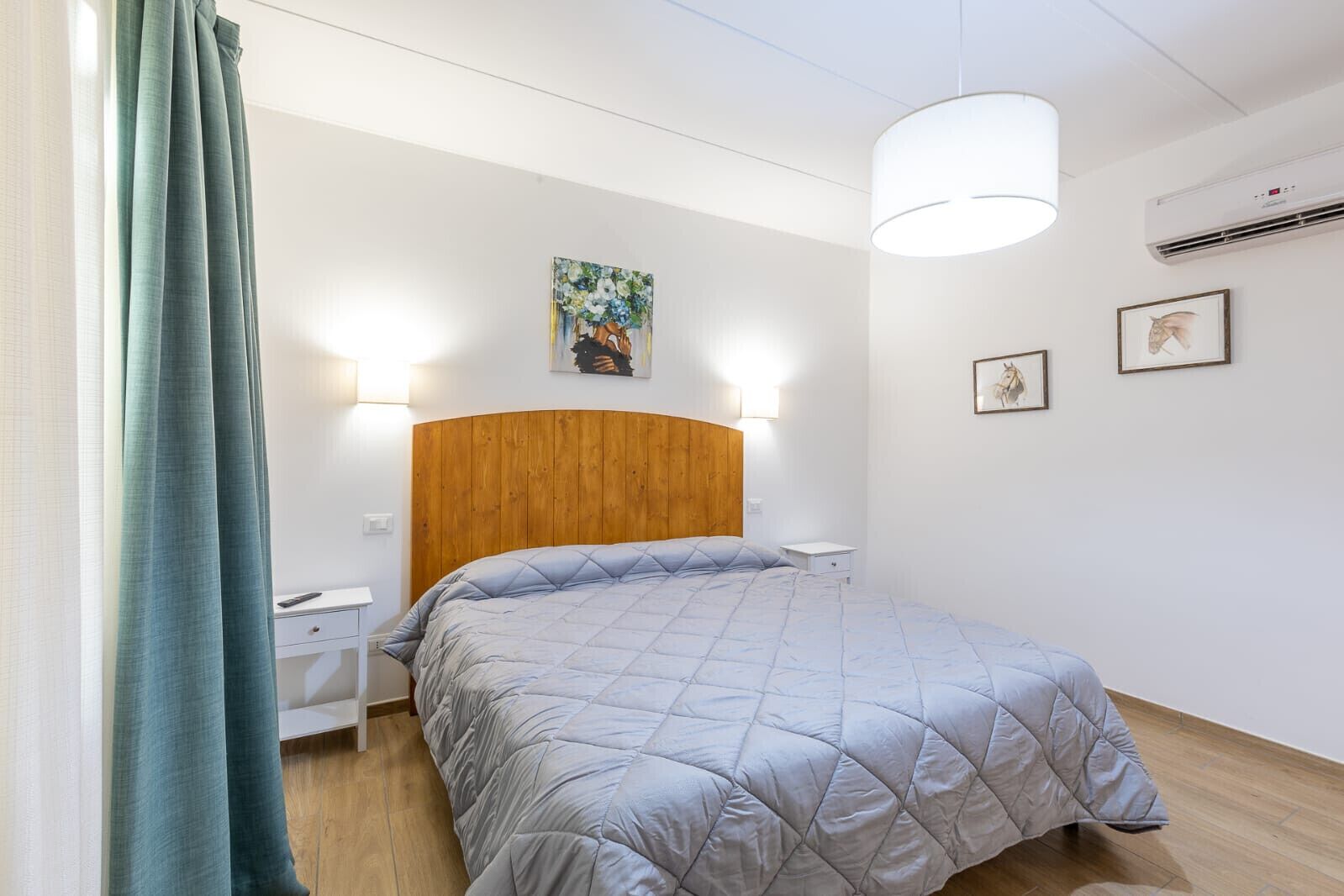 A bedroom with a wooden headboard, a bed with a quilted blanket, bedside tables, wall-mounted lights, and a painting.