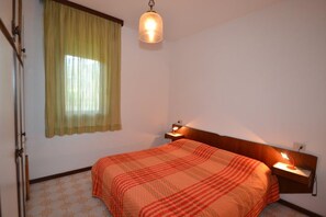 Una camera da letto con un letto, un comodino, una lampada, una finestra con tende e una lampada a sospensione.