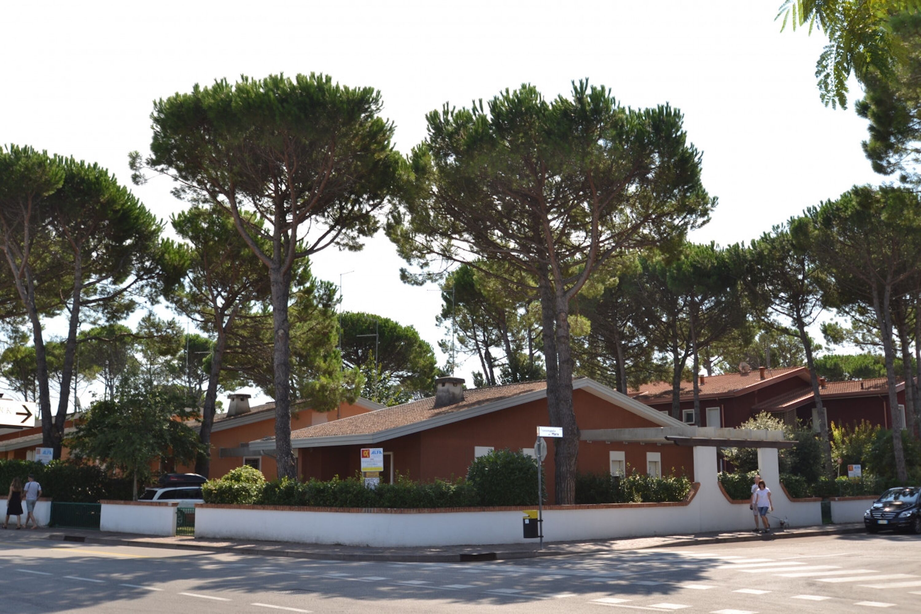 Un bâtiment avec un toit rouge, entouré d’arbres et bordé d’un mur blanc.