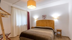 A bedroom with a wooden headboard, a bed with a brown blanket, two bedside tables, a hanging lamp, and a window with curtains. - Le Vigne - Appartamento Palazzo Chiavoni (Bolsena)
