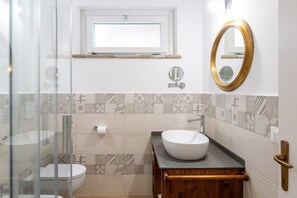 Ein Badezimmer mit Duschkabine aus Glas, Toilette, Waschbecken mit Aufsatzbecken, Waschtisch mit Holdekor, spiegel mit goldfarbener Rahmen und Wandfliesen mit Muster.