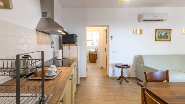 A kitchen with a microwave, stove, and a coffee maker on the counter. There is a dining table with chairs and a small round table with a lamp. - Le Vigne - Appartamento Palazzo Chiavoni (Bolsena)