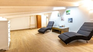 A spacious room with wooden flooring, a ceiling with exposed beams, a wooden wardrobe, a small table with a lamp, and two lounge chairs. - Le Vigne - Appartamento Giardini (Bolsena)