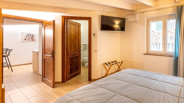 A bedroom with a bed, a TV, a window, and a door leading to a bathroom. - Le Vigne - Appartamento Giardini (Bolsena)