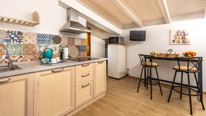 A kitchen with a microwave, kettle, and coffee maker, a dining area with two chairs, and a TV on the wall. - Le Vigne - Appartamento Giardini (Bolsena)