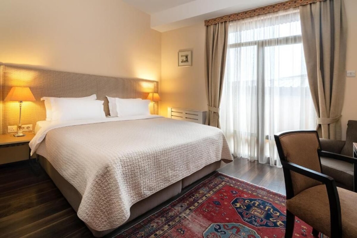 A hotel room with a large bed, two bedside lamps, a chair, and a window with curtains.