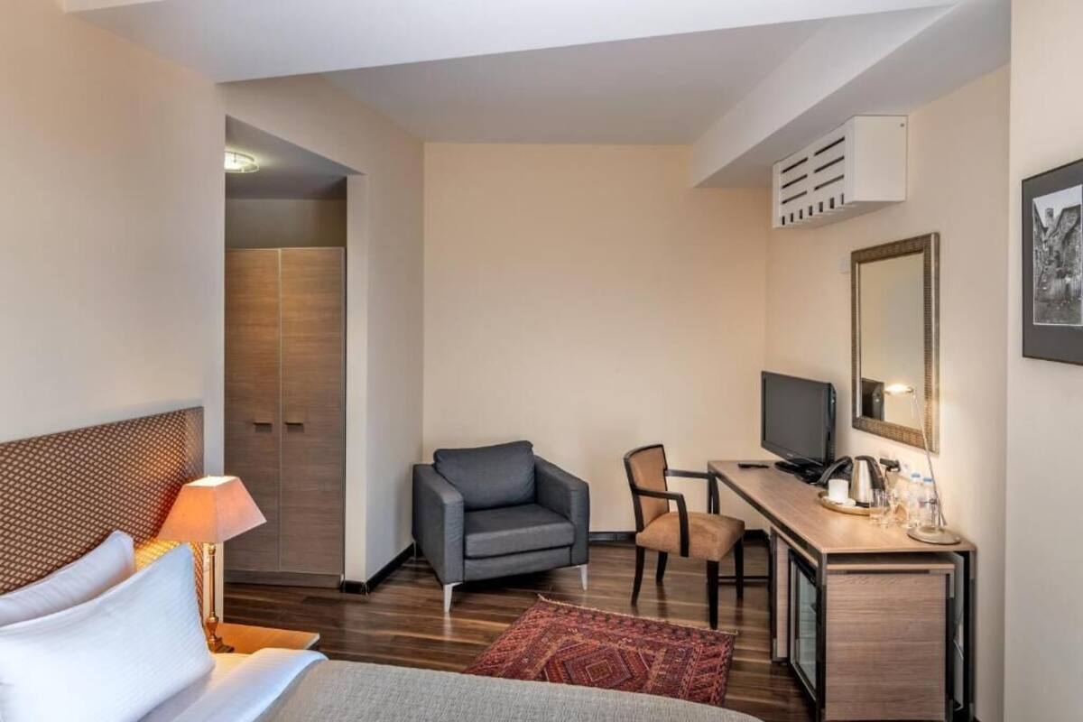 A hotel room with a bed, a desk with a TV, a chair, a small table, and a mirror.