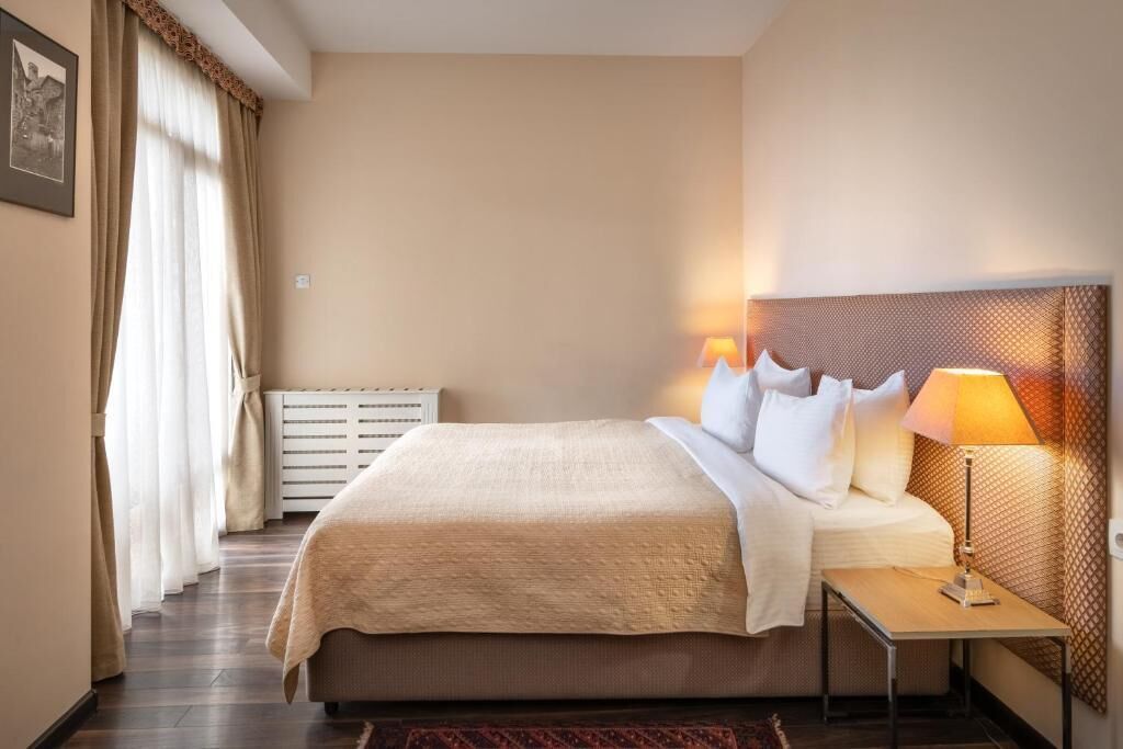A hotel room with a bed, bedside table, lamp, and a radiator.