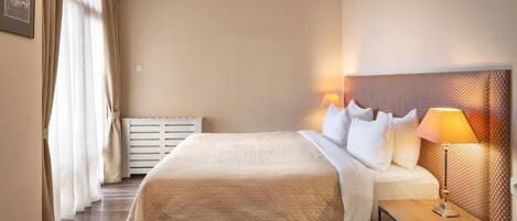 A hotel room with a bed, bedside table, lamp, and a radiator.