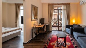 A room with a bed, desk, and seating area, a balcony with a railing, and a window with curtains. - Ginger Hotel (Tbilisi)