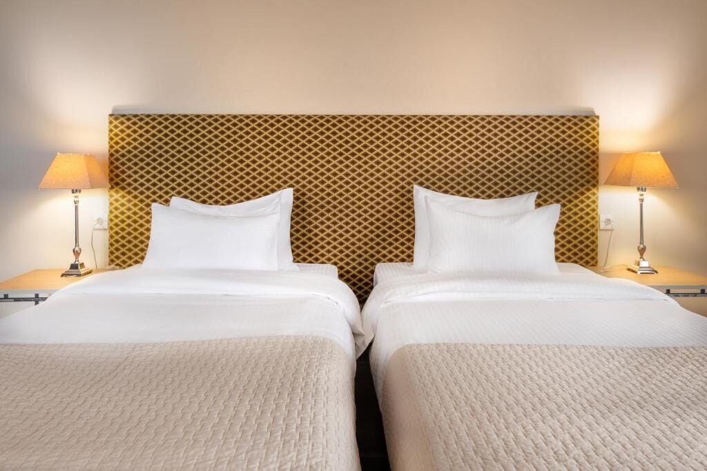 A hotel room with two beds, a patterned headboard, bedside lamps, and a neutral color scheme.