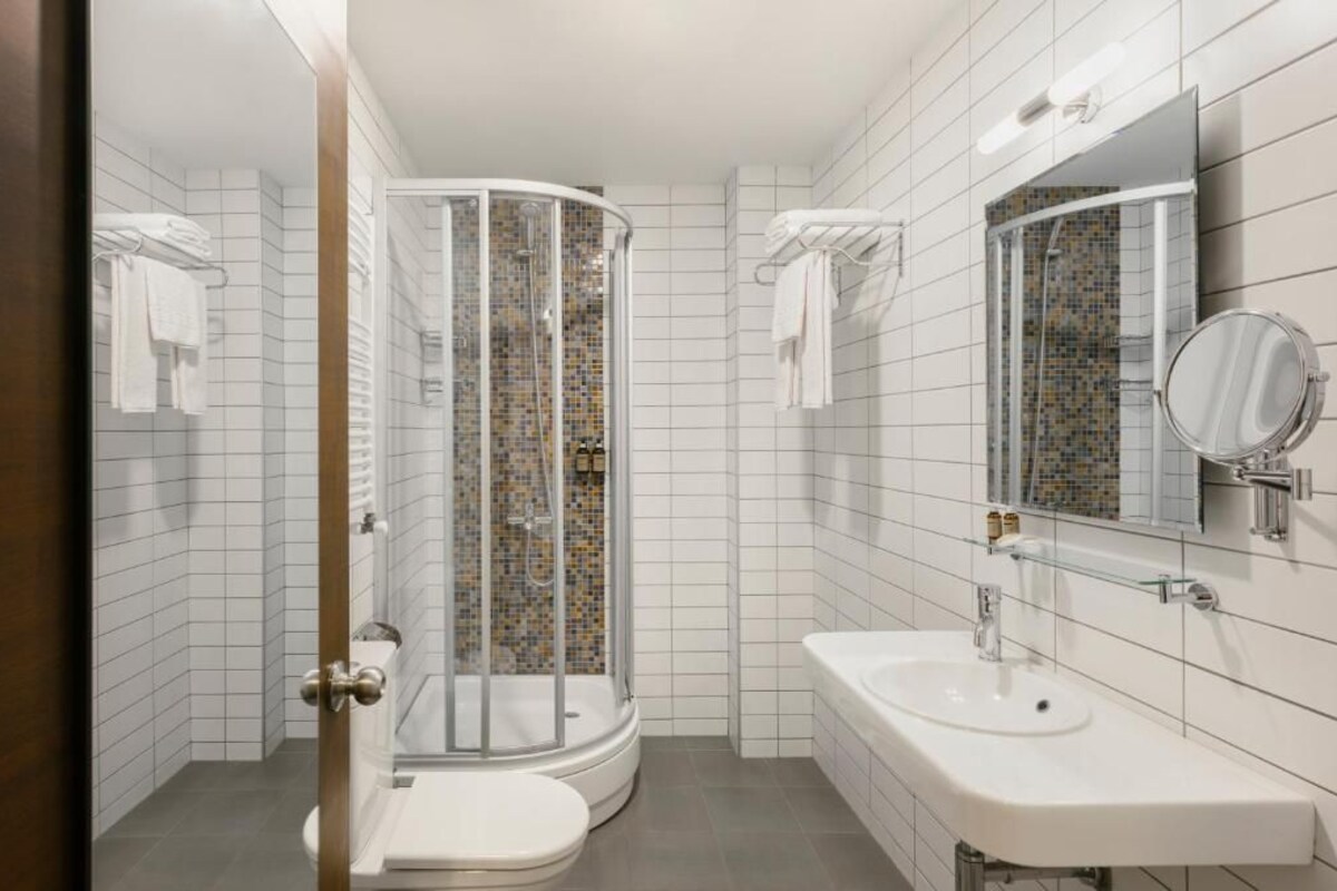 A bathroom with a shower, toilet, sink, and a mirror.