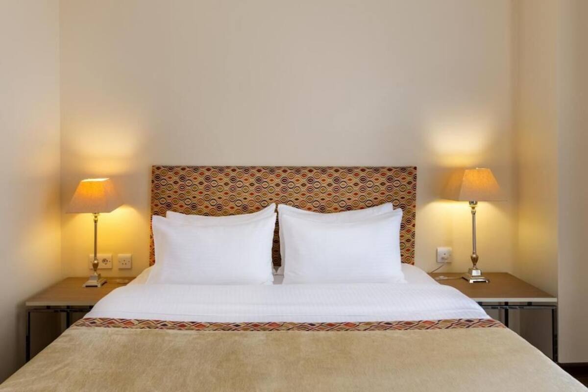 A bed with a patterned headboard, two bedside lamps, and a decorative border at the foot of the bed.