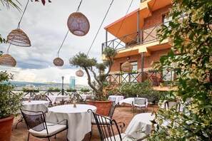 An outdoor patio with round tables and chairs, a brick building, and hanging wicker lamps. - Ginger Hotel (Tbilisi)