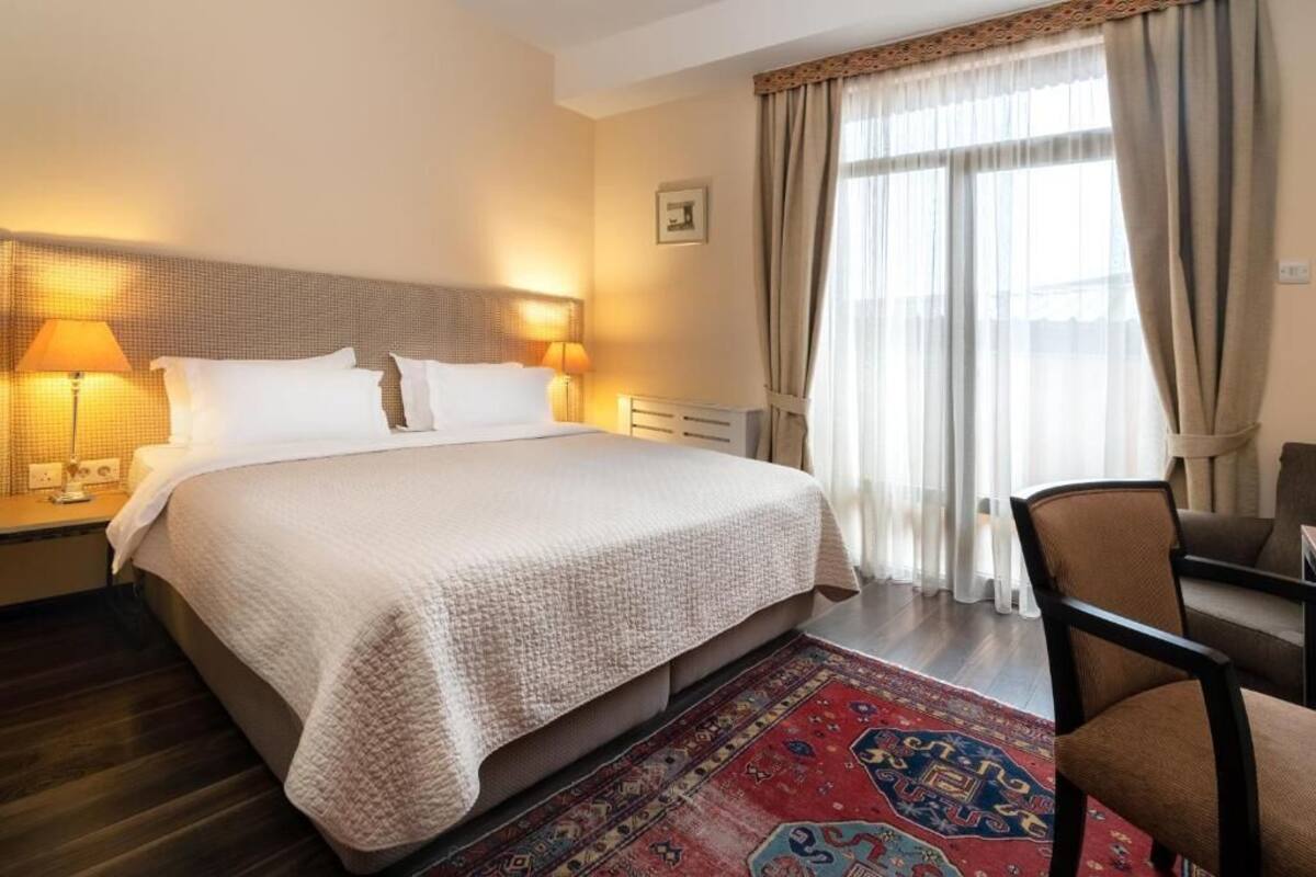 A hotel room with a large bed, two bedside lamps, a chair, and a window with curtains.