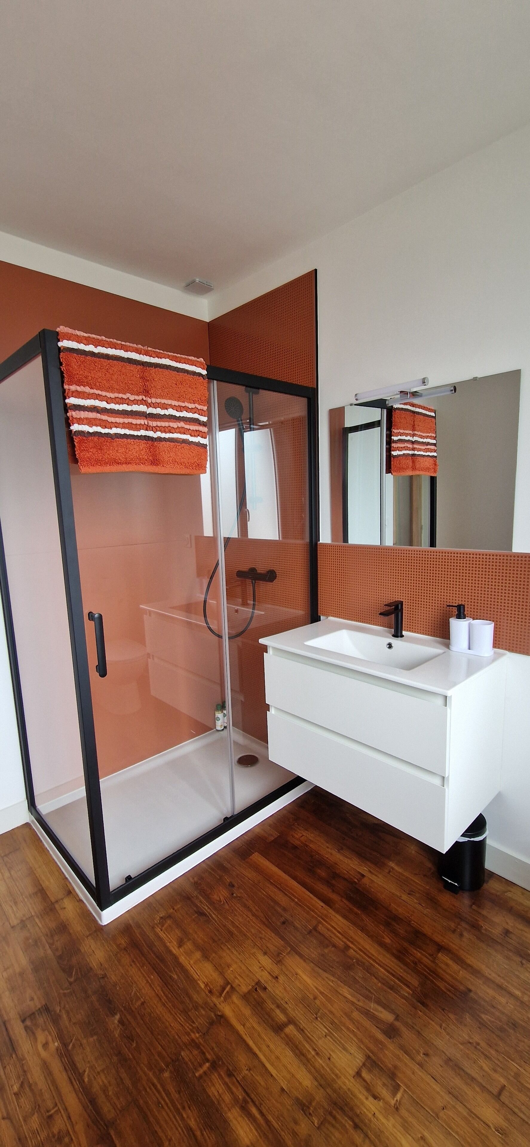 Un baño moderno con ducha envuelta en vidrio, un tocador blanco con grifo negro y un espejo sobre el lavamanos.