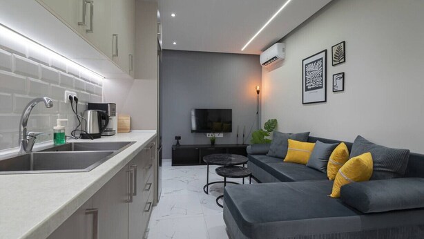 A modern kitchen with a built-in oven, a dining area with a sofa and coffee table, and a flat-screen TV mounted on the wall. - Central Cozy Home by Rentals Pro - Nea Moudania Halkidiki (Nea Moudania)