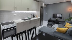 A modern kitchen with white cabinets, a built-in oven, and a dining area with a gray sofa and yellow cushions. - Central Cozy Home by Rentals Pro - Nea Moudania Halkidiki (Nea Moudania)