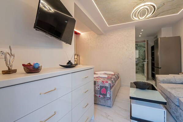 A modern bedroom with a TV, a bed, a dresser, and a small table.